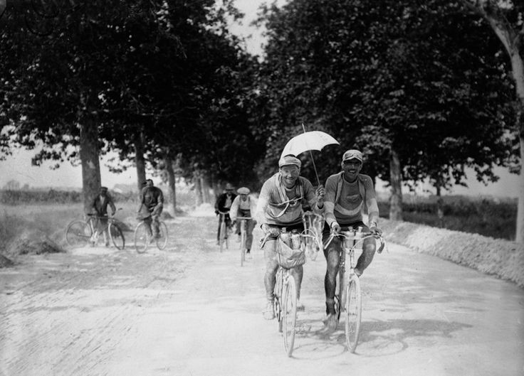Two cyclists riding on the dusty road at the Tour de France in 1923, one of them is holding an umbrella