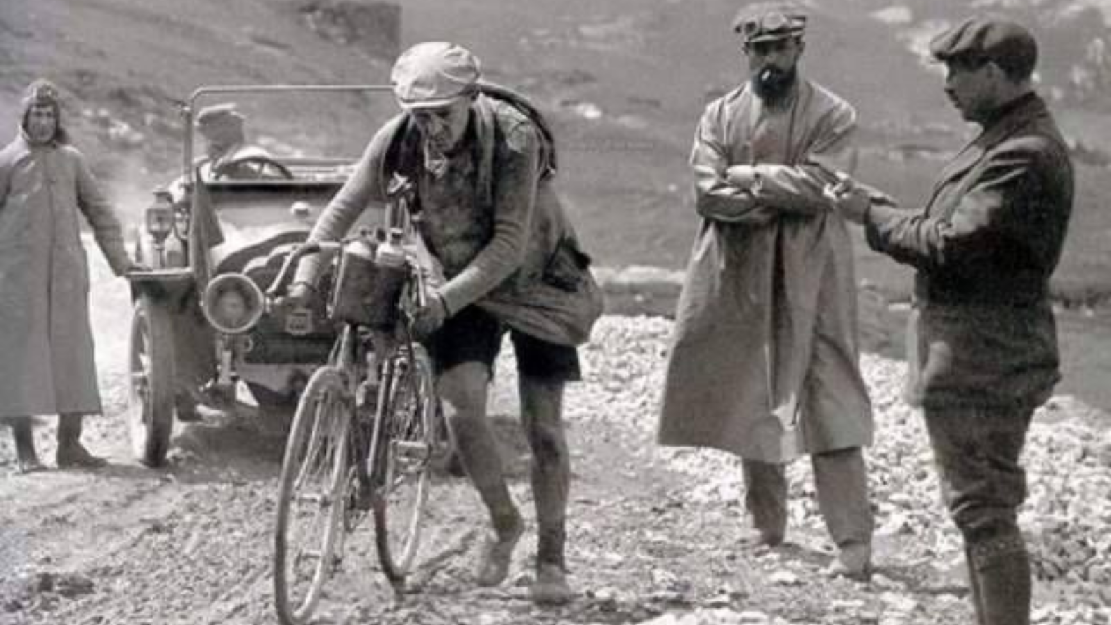Black and white picture about Octave Lapize, a sole cyclist, on foot, cresses the Tourmalet while teo other people watching him.