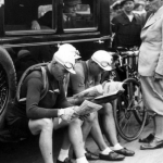 Black and white vintage picture about cyclists sitting at the side of a car and reading newspaper at the Tour de France 1931