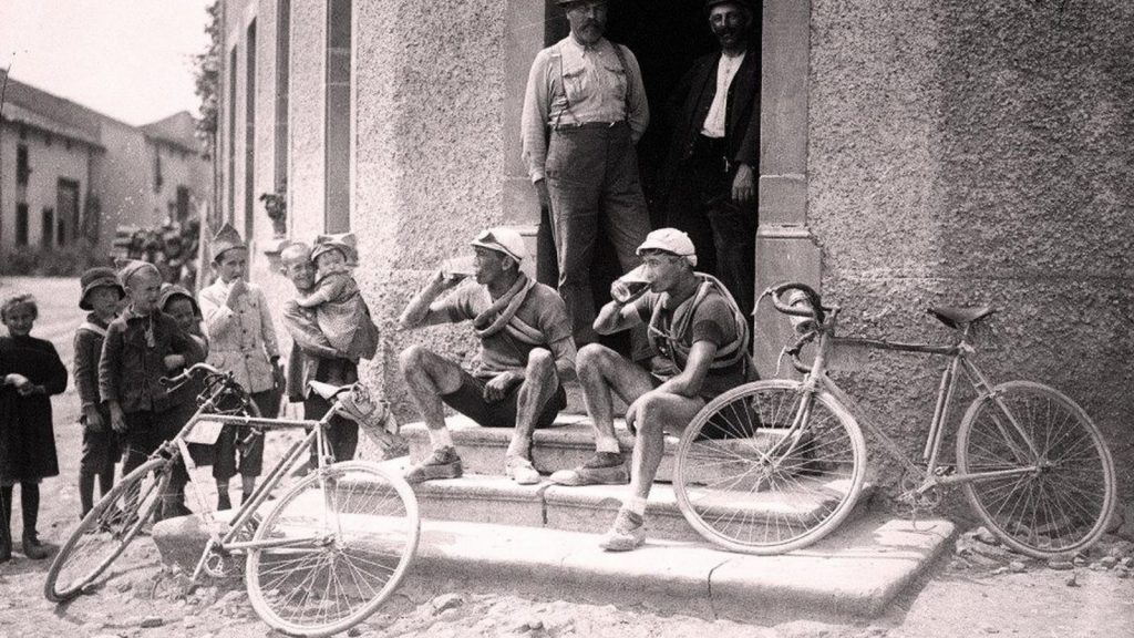 Two cyclists sitting on the steps of a tafern and drinking beer at Tour de France 1921