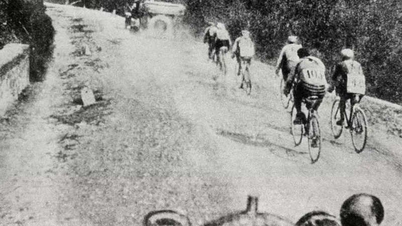 A bunch of cyclists are riding on the unpaved road during the first Giro d'Italia in 1909.